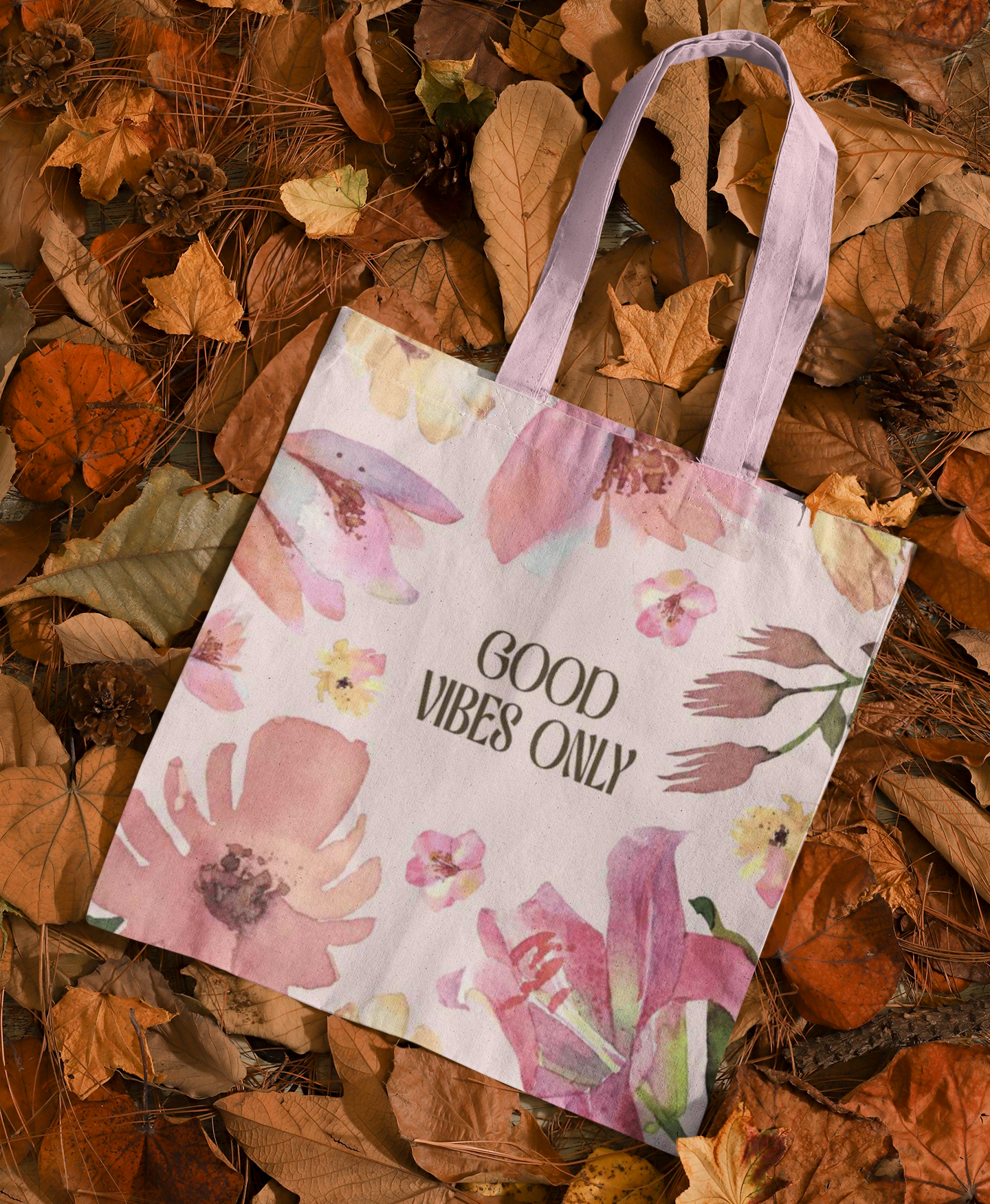 Floral tote bag with 'Good Vibes Only' text on a bed of autumn leaves